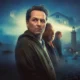 Promotional image for the Apple TV+ series Widow's Bay. A man in a dark hoodie stands in the foreground, looking wary, with an older man and a young woman behind him. A misty coastal scene surrounds them, featuring a lighthouse beam cutting through fog, a house with lit windows, and a small boat on dark water under a full moon. The Horrortainment News logo appears in the lower right corner.
