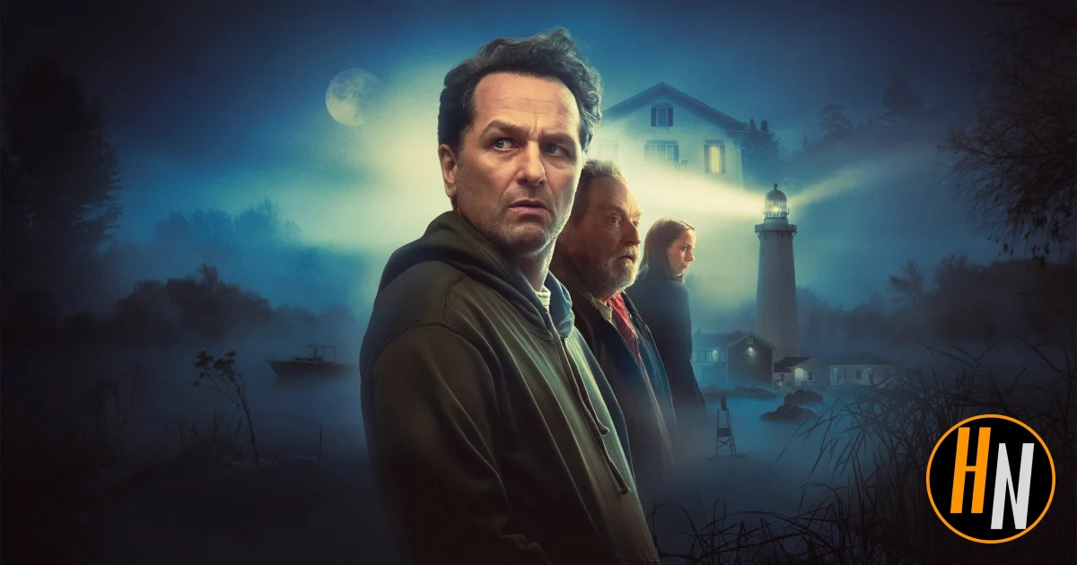 Promotional image for the Apple TV+ series Widow's Bay. A man in a dark hoodie stands in the foreground, looking wary, with an older man and a young woman behind him. A misty coastal scene surrounds them, featuring a lighthouse beam cutting through fog, a house with lit windows, and a small boat on dark water under a full moon. The Horrortainment News logo appears in the lower right corner.
